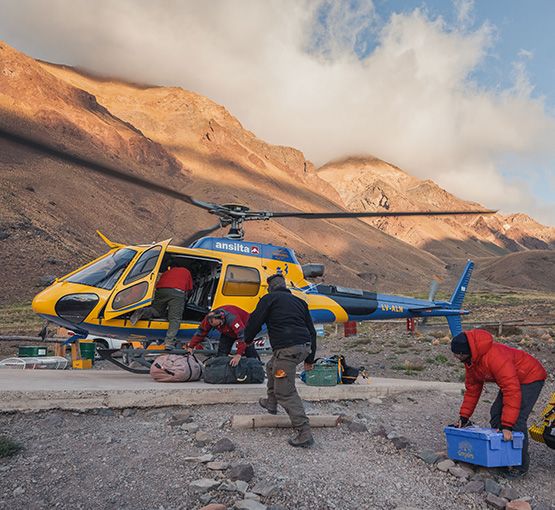 Helicopter at Aconcagua camp for expedition logistics with mountains in background