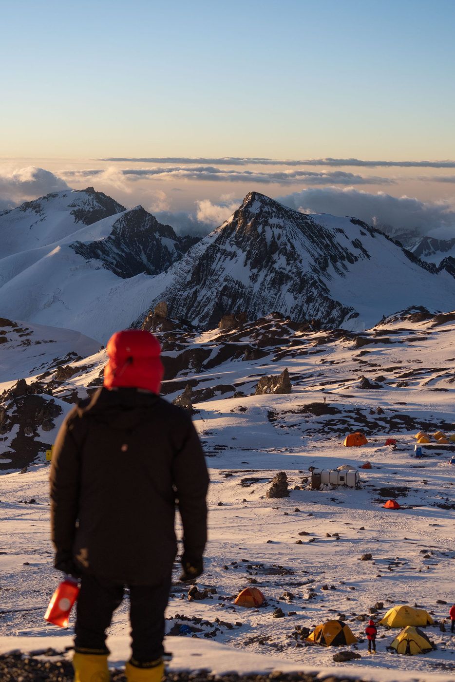 Climber at camp looking over clouds and peaks at sunrise on Aconcagua