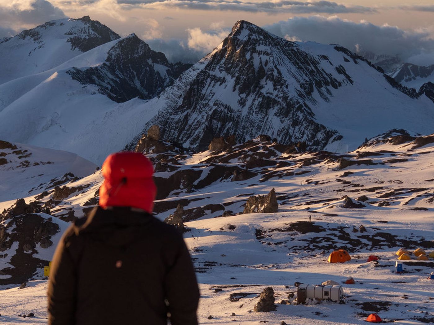 Climber at camp looking over clouds and peaks at sunrise on Aconcagua
