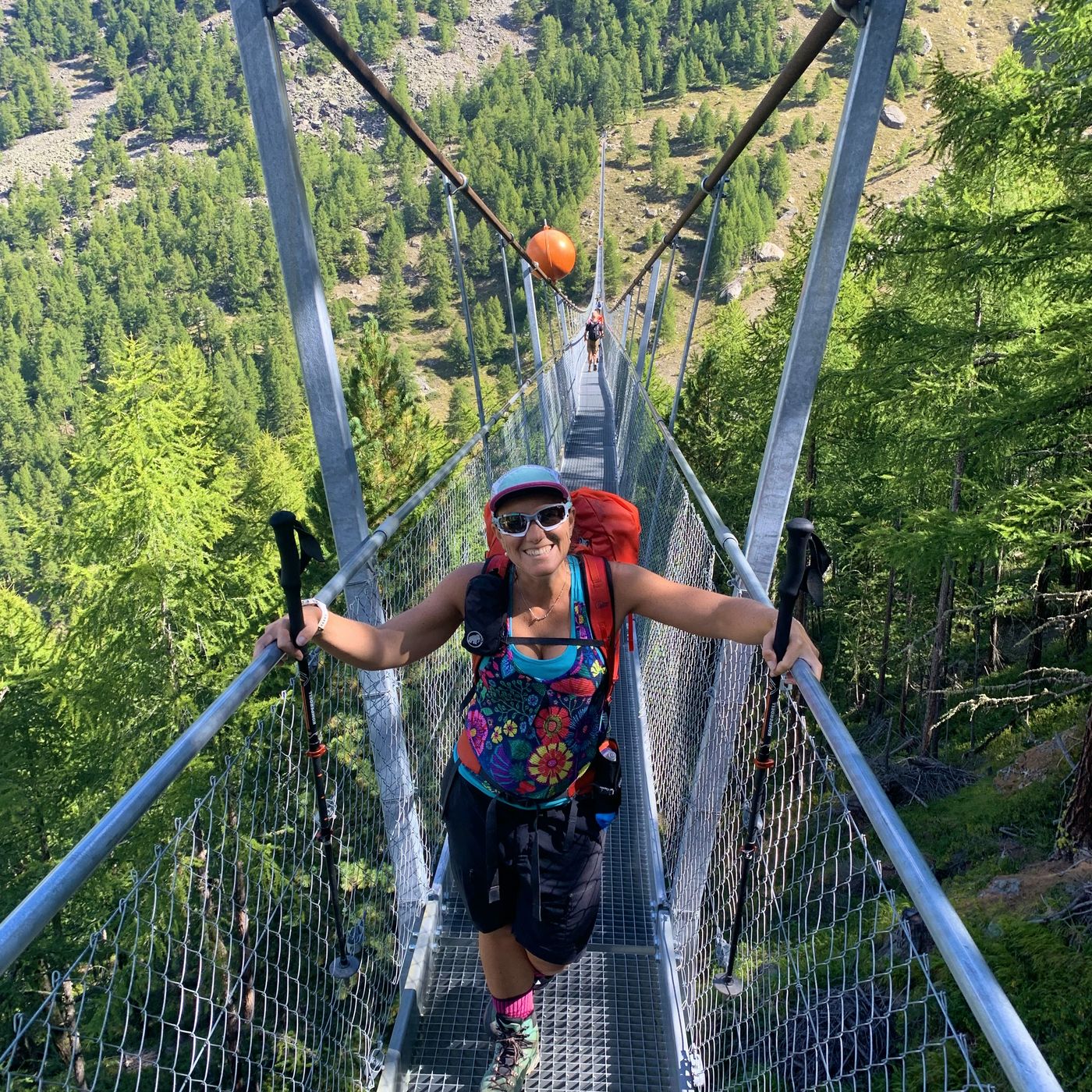 Hiker crossing a suspension bridge with lush forest valley below