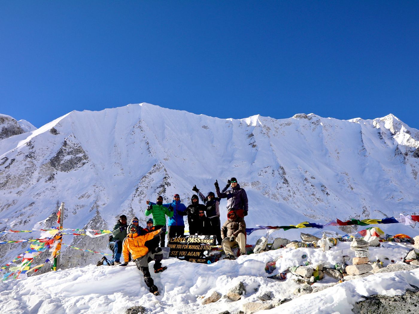 Trekkers resting outside a high mountain teahouse with prayer flags