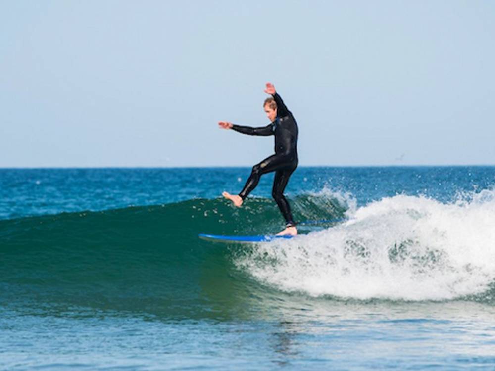 Surfers riding waves at Fistral Beach Cornwall during surf camp lesson with surfboards and wetsuits