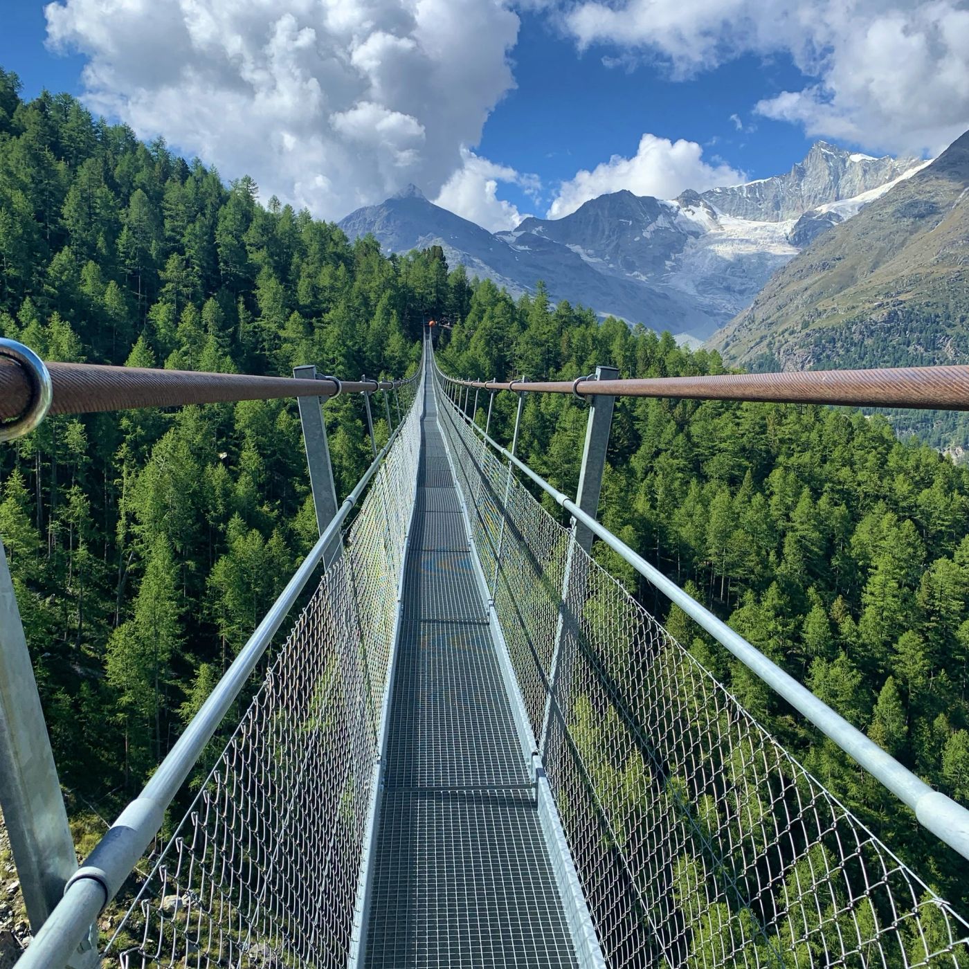 Charles Kuonen suspension bridge stretching toward snow-capped peaks above pine forest