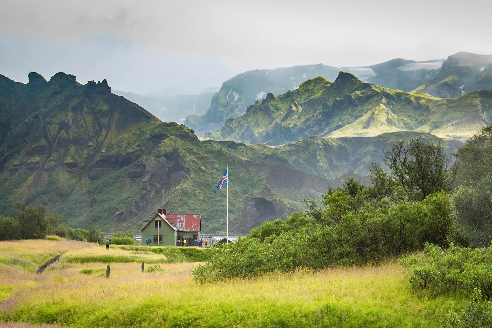 Hikers trekking through dramatic Icelandic highlands on Laugavegur Trail with colorful rhyolite mountains, volcanic landscape, and glacier valleys