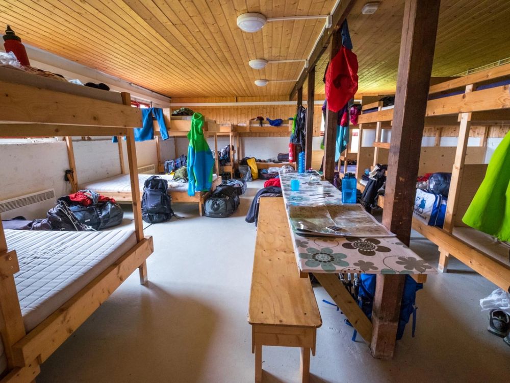 Warm mountain hut interior with bunks, camping gear, and cozy shared seating area