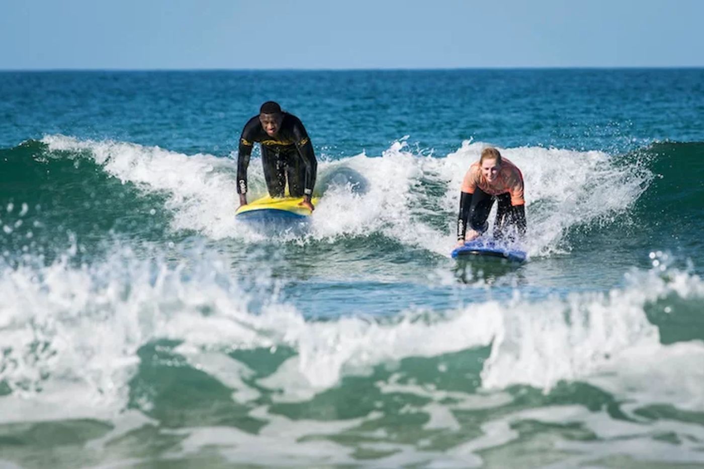 Happy surfers in wetsuits smiling and splashing in the Cornish sea.