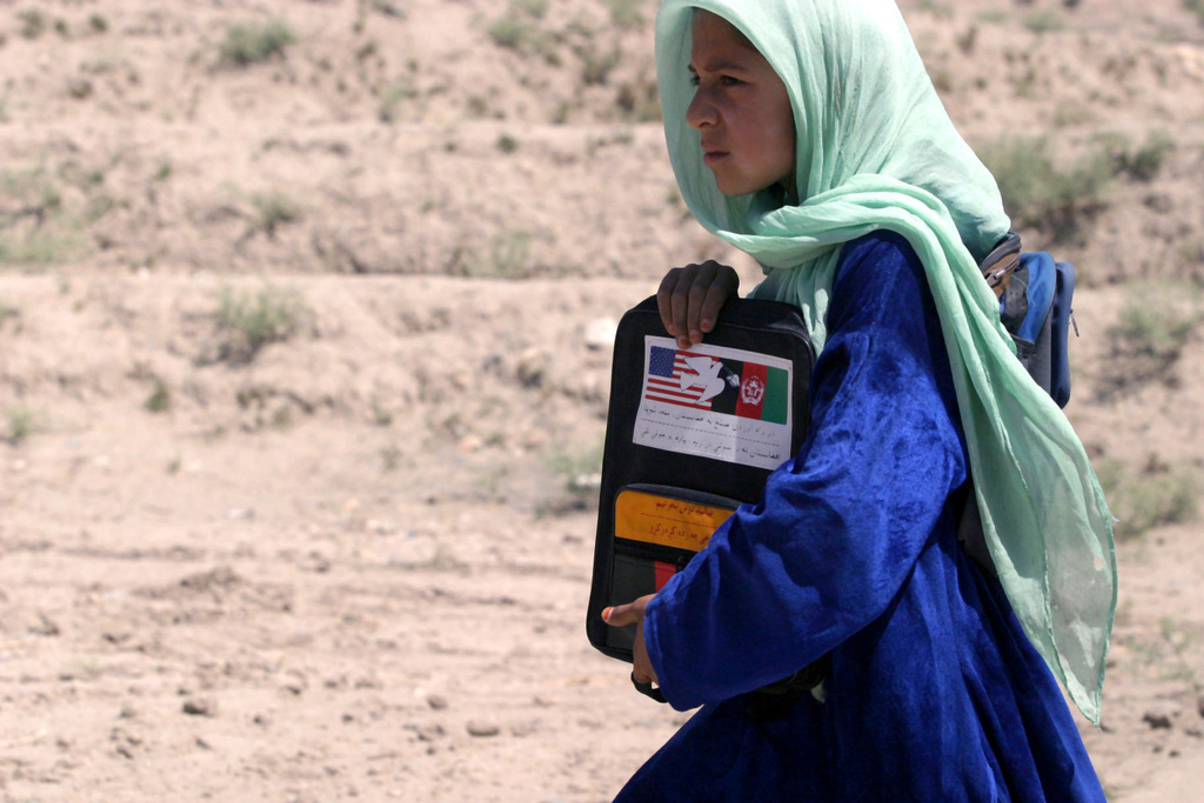 Afghan girl holding school materials in a rural setting amid education crisis.