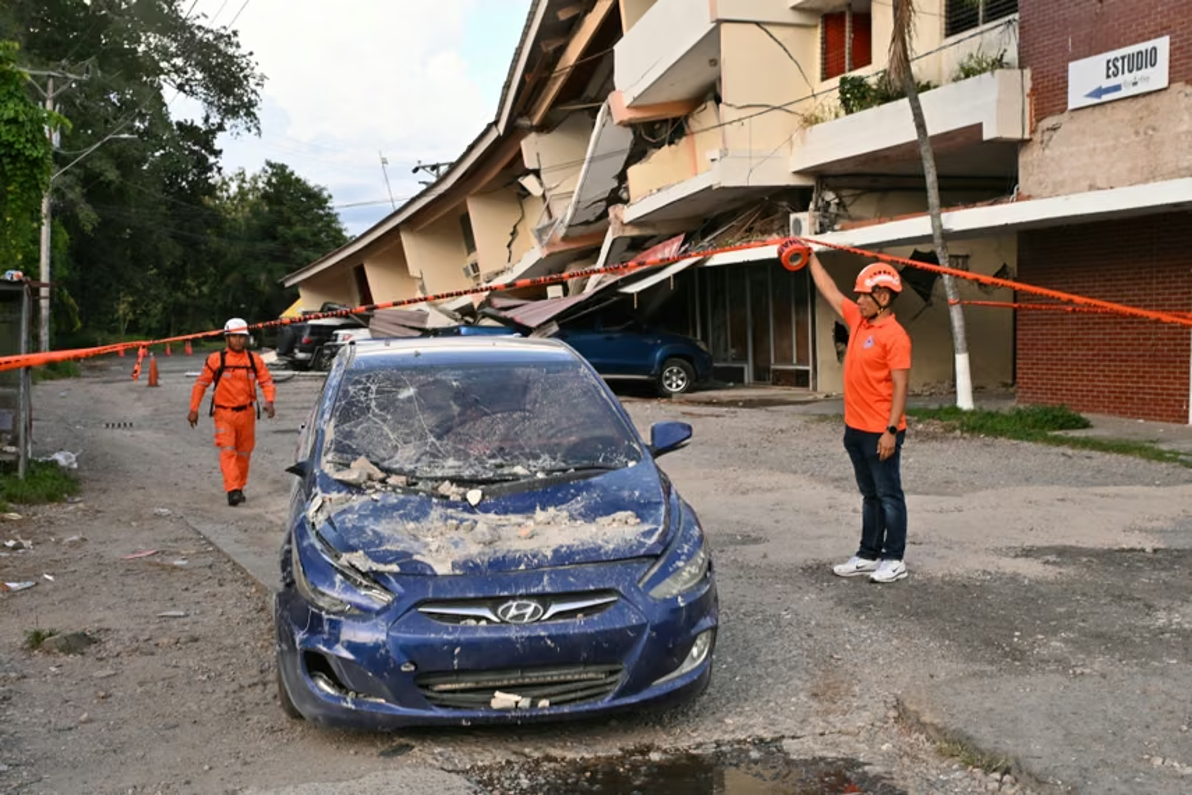Rescue workers tape off a partially collapsed building and a debris-covered car after the 2026 Panama earthquake.