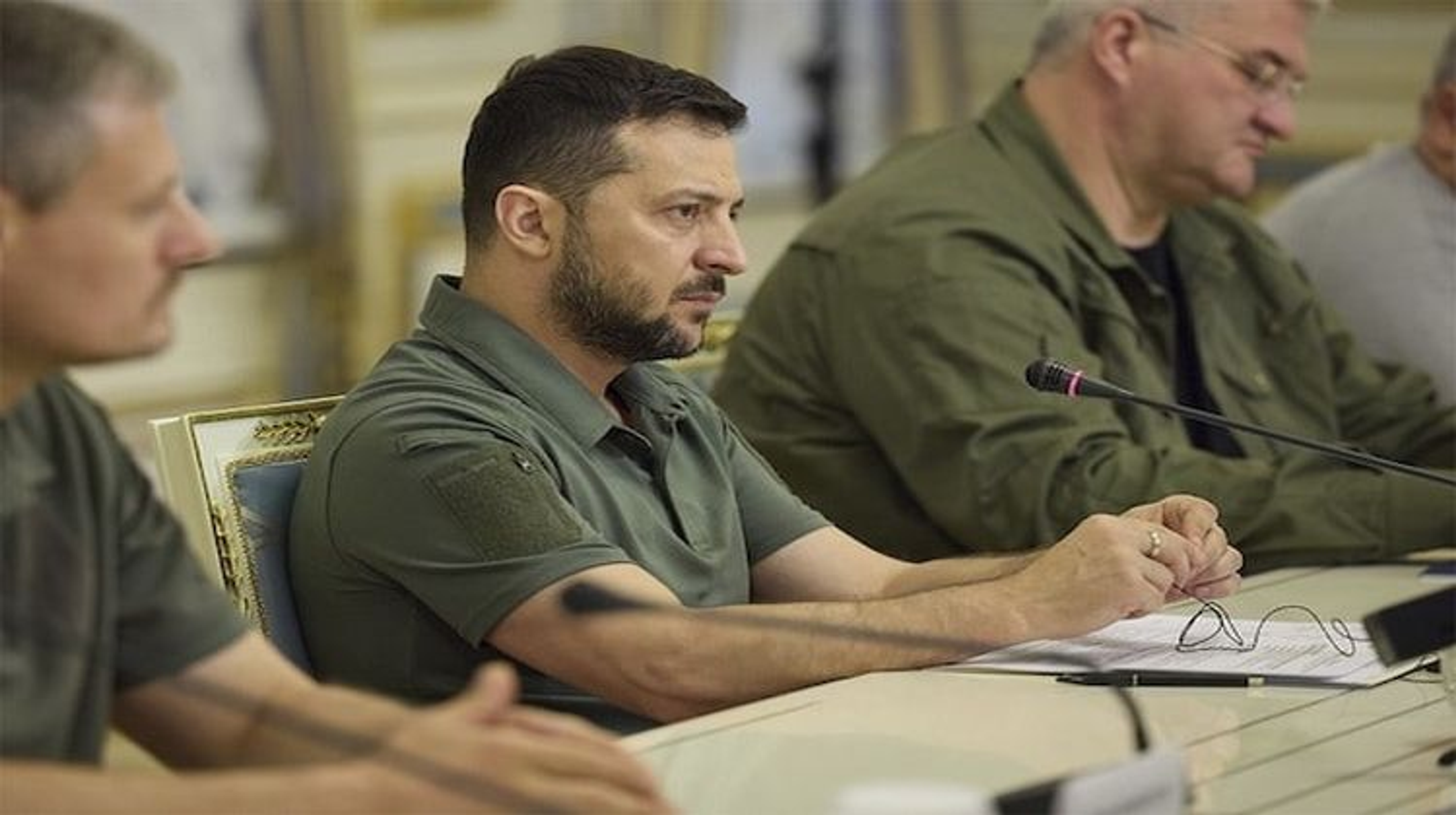 Volodymyr Zelenskyy in a meeting with officials, seated at a conference table with a microphone.