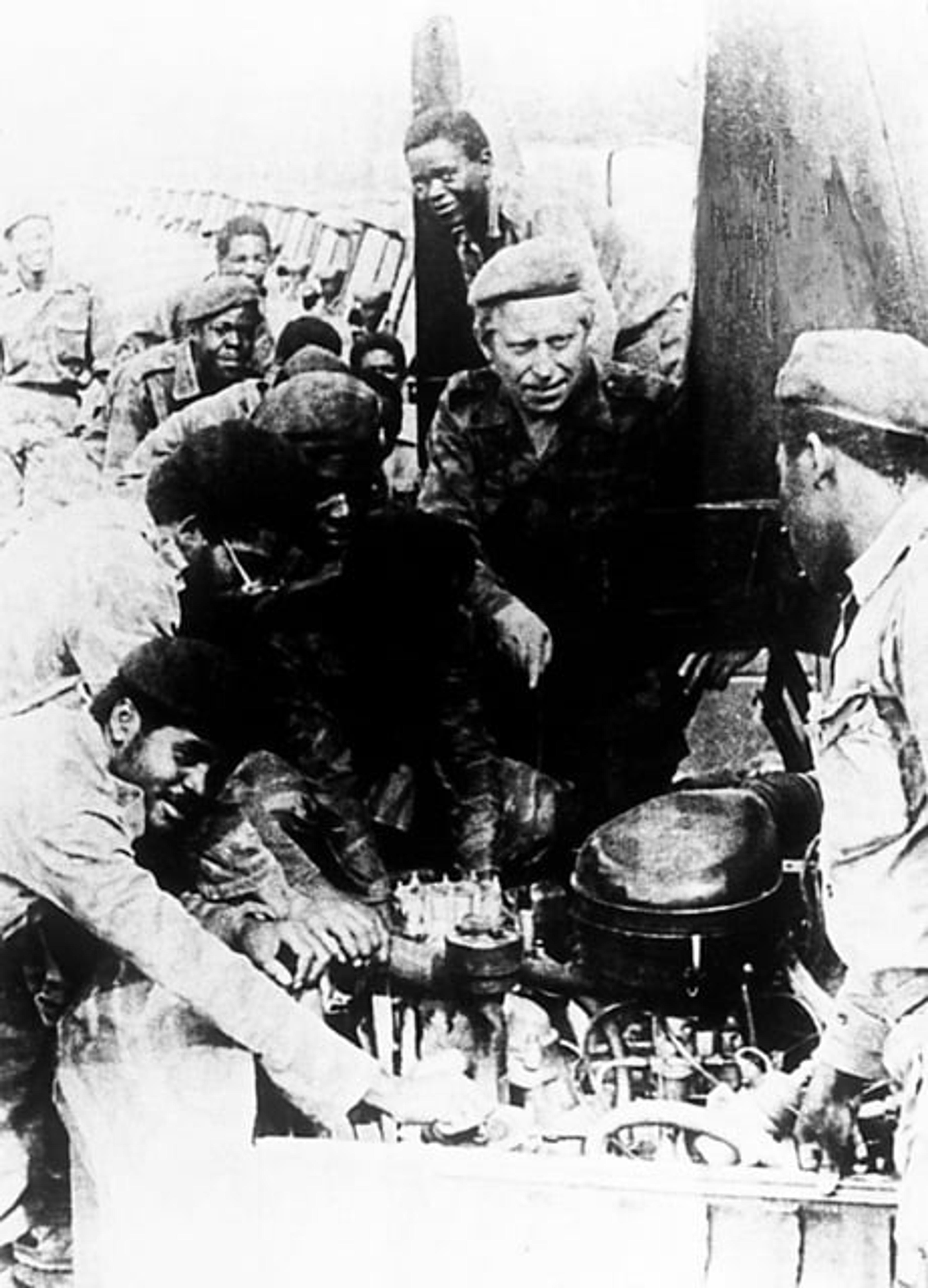 Grupo de soldados reunidos alrededor del equipo durante un conflicto, recibiendo orientación técnica.