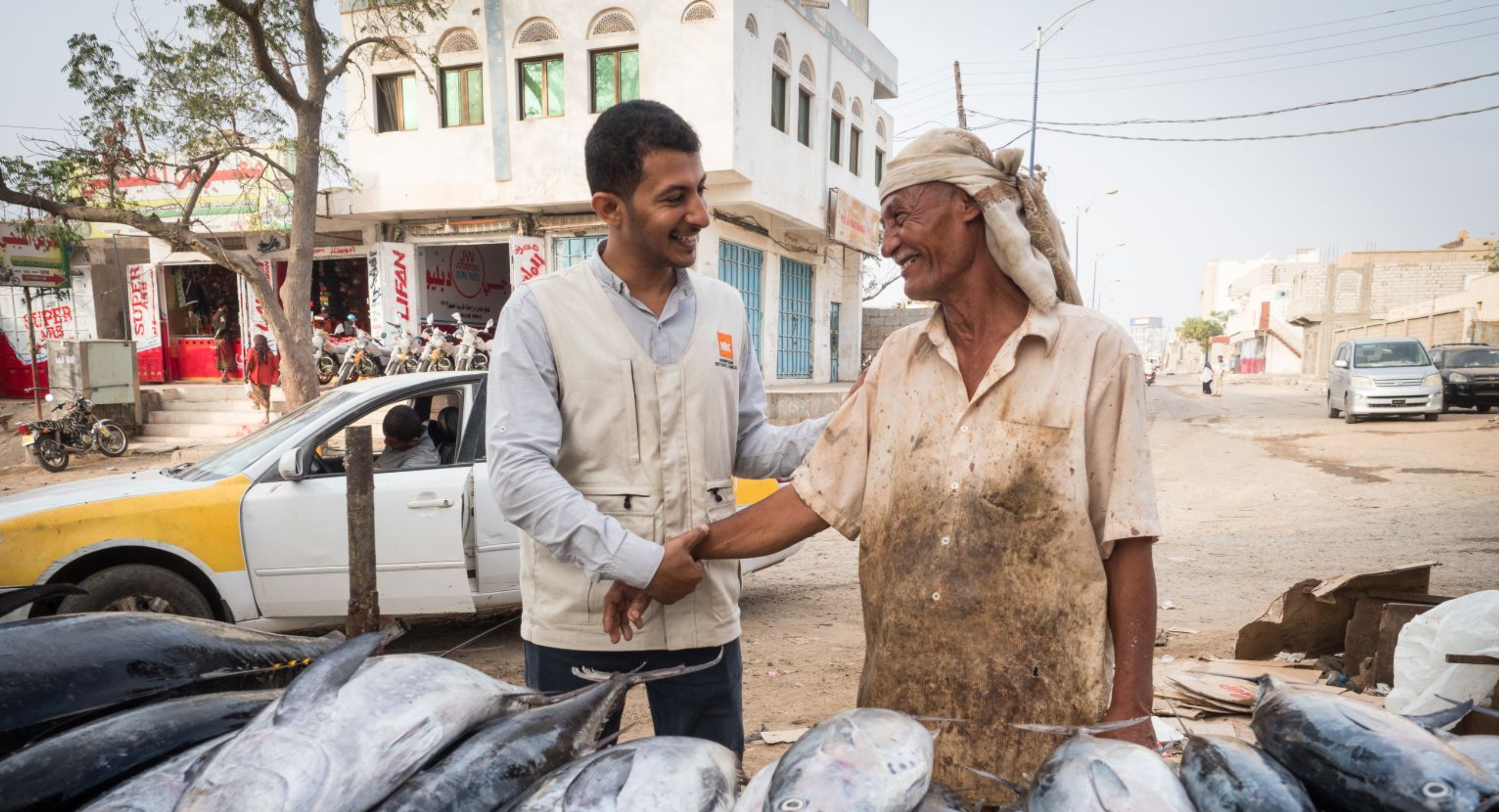 Aid worker shakes hands with a smiling fisherman at a fish market in Yemen.