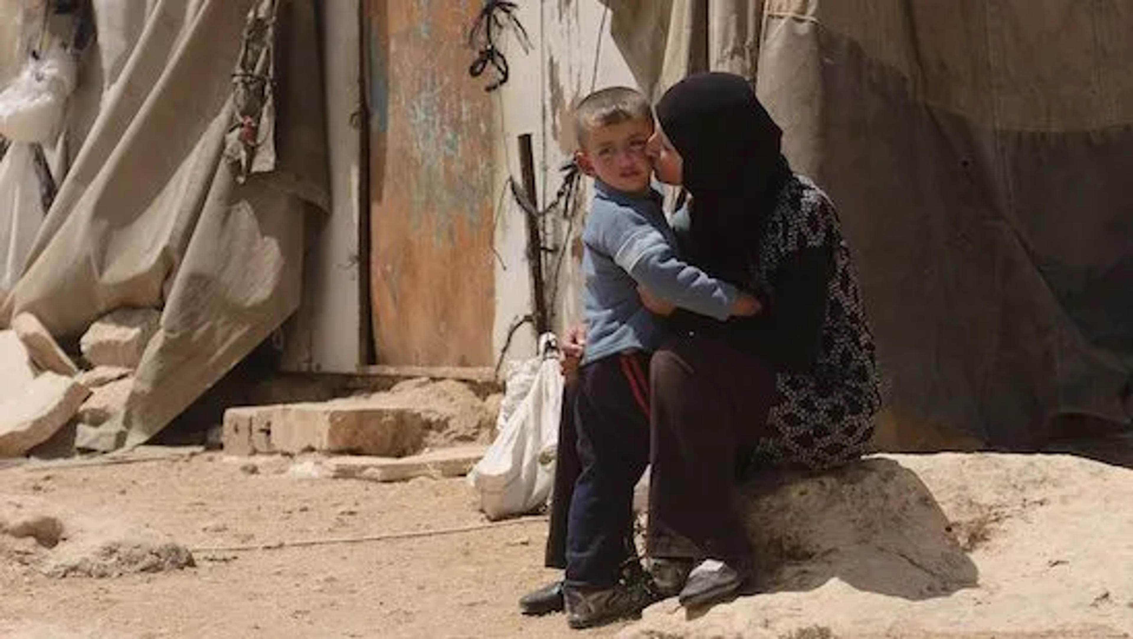 Woman in hijab kissing a boy in a refugee camp.