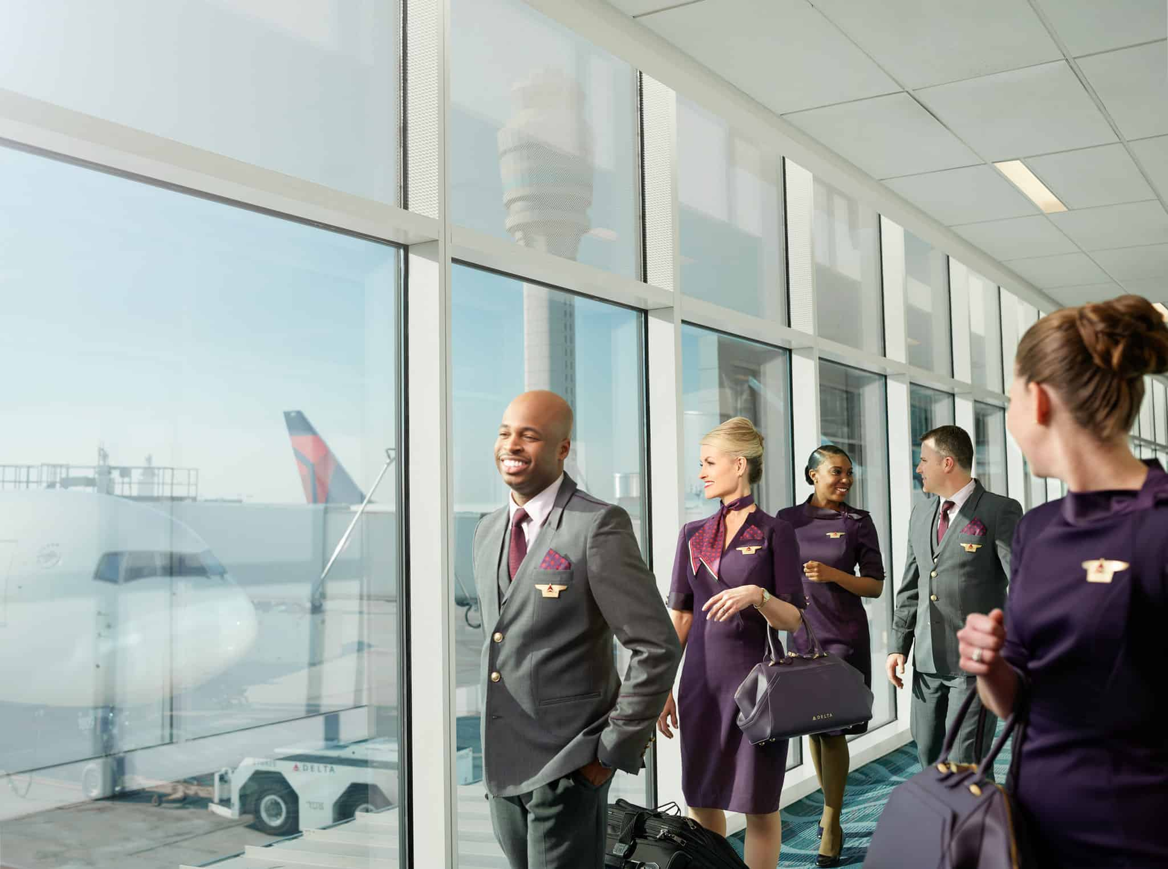 Delta flight crew walking through an airport terminal with an aircraft visible outside.