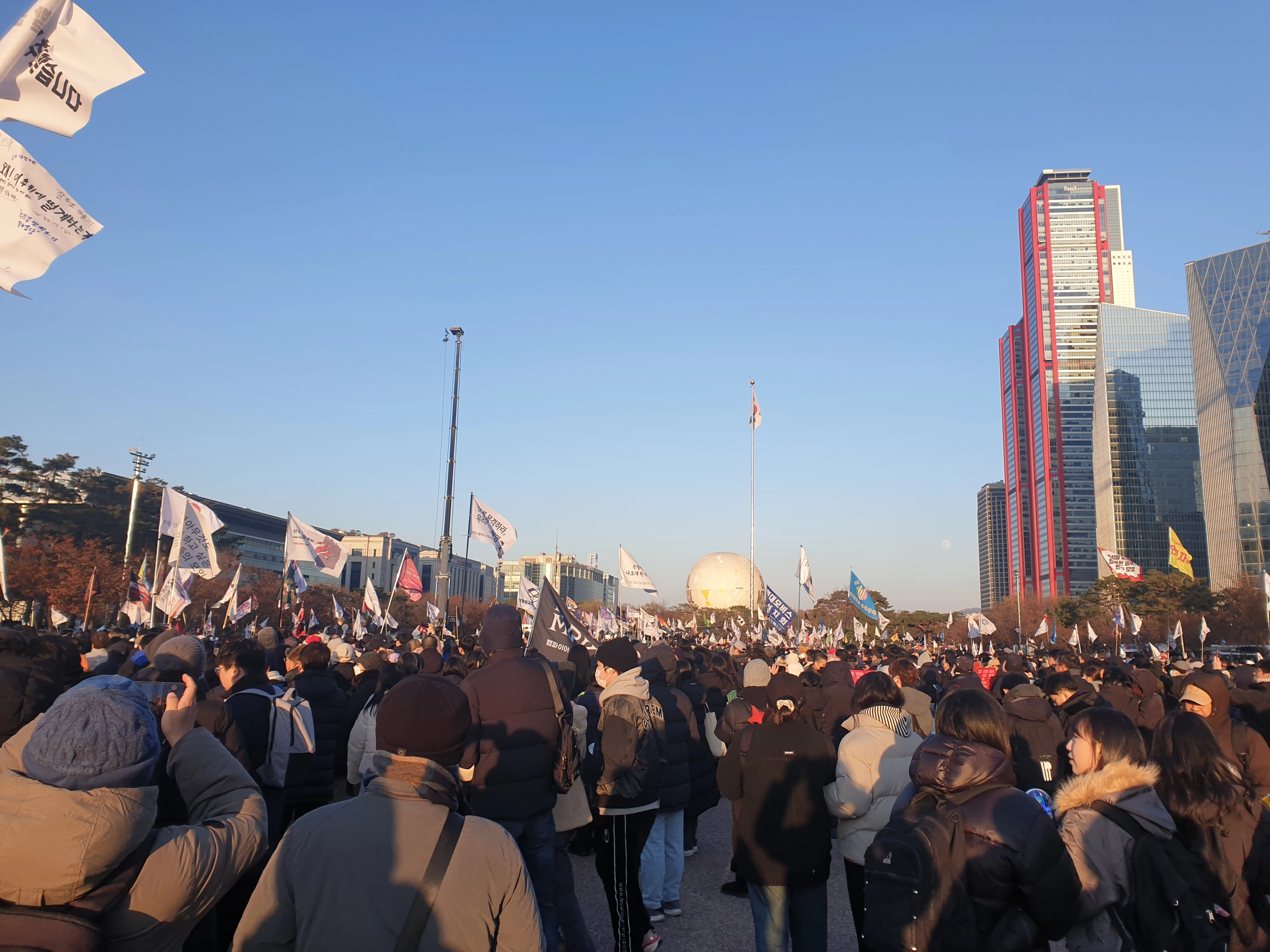 Gran manifestación pública en Seúl, Corea del Sur, con manifestantes sosteniendo banderas cerca de los rascacielos de la ciudad.