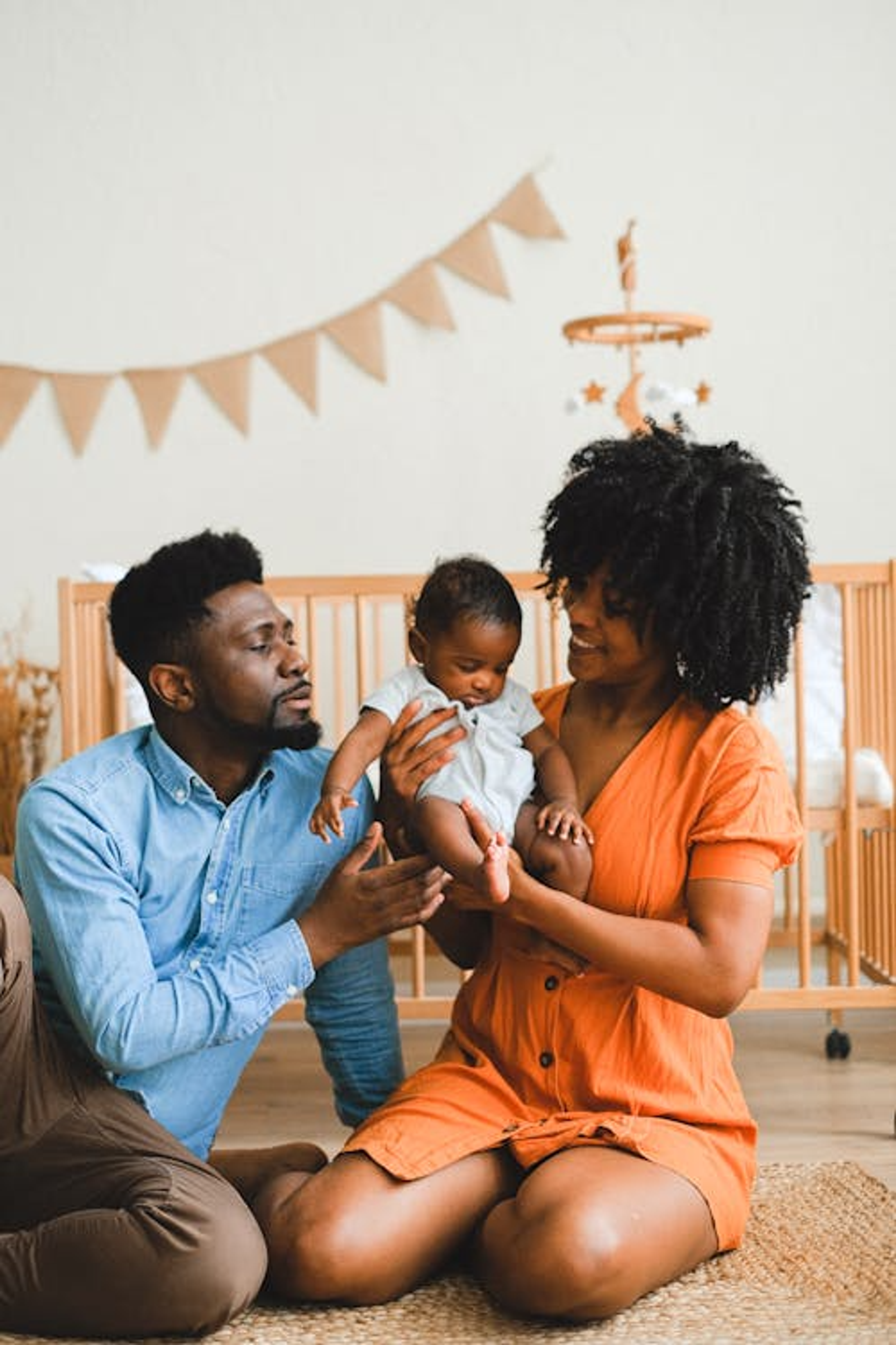 Padres negros sentados en el suelo, sosteniendo con amor a su bebé en una guardería.