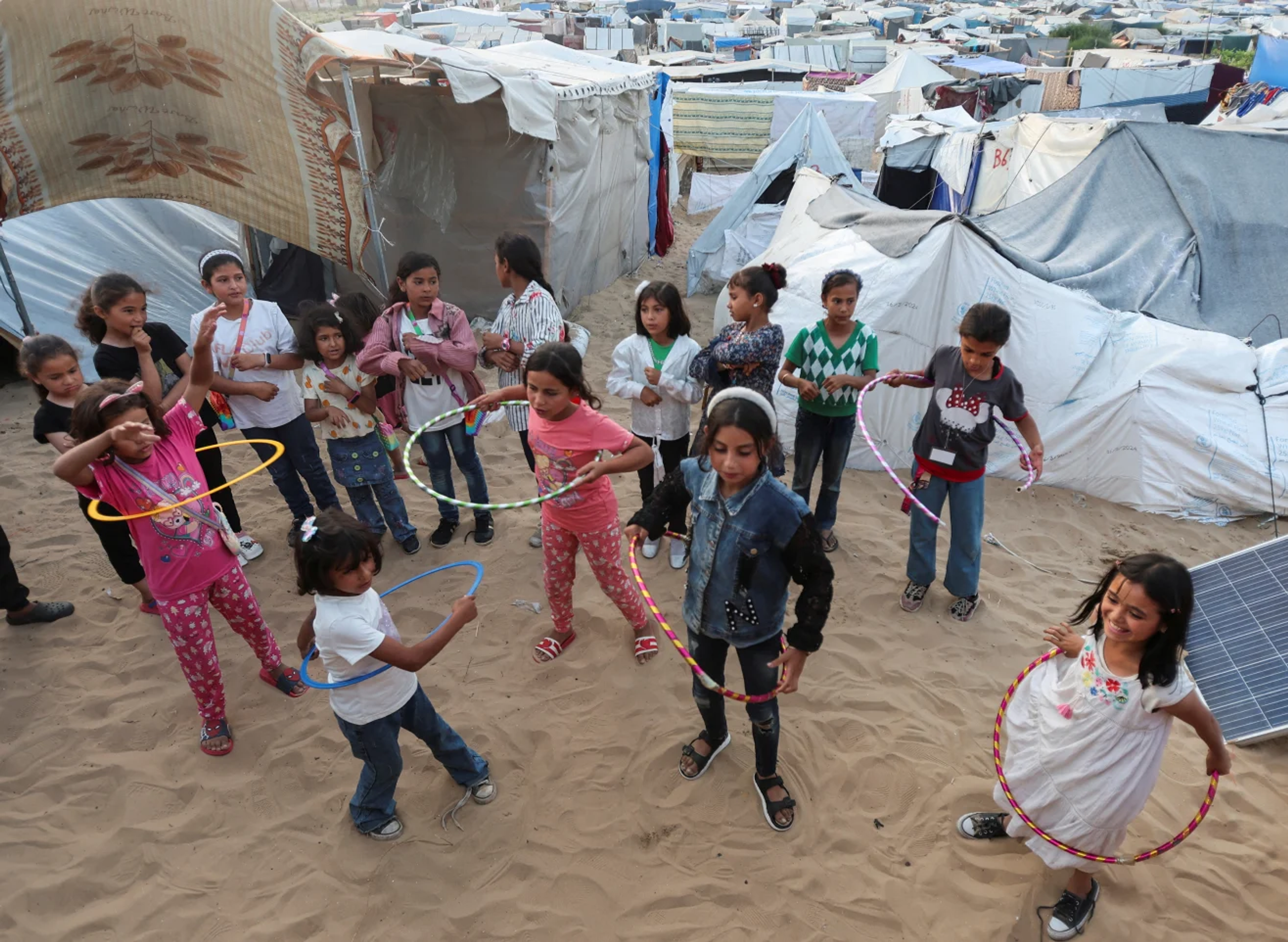Displaced children playing with hula hoops in a temporary camp.