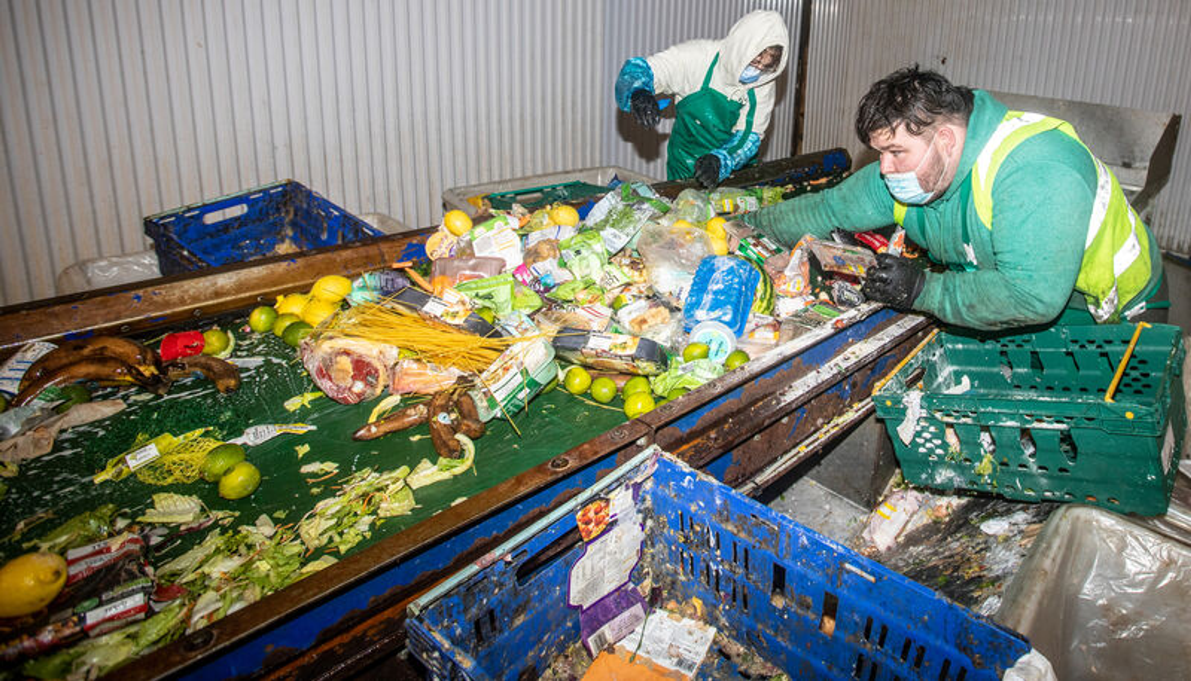 Des travailleurs triant des aliments jetés et des produits d'épicerie emballés sur un tapis roulant dans une installation de traitement des déchets.