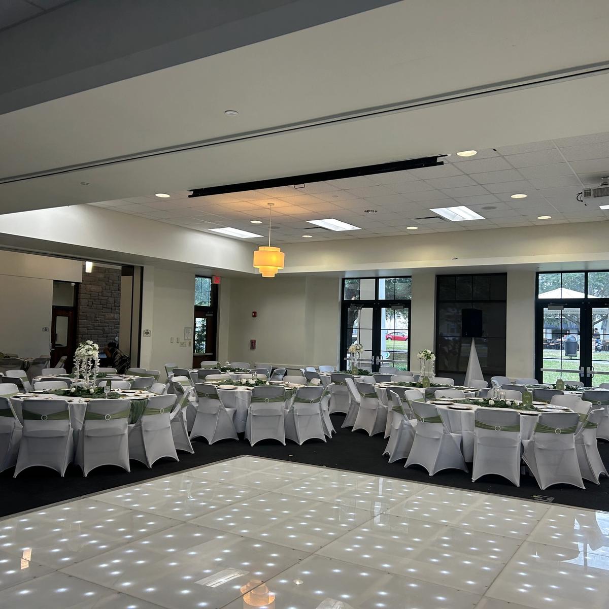 White chair covers with sage sashes around an LED dance floor