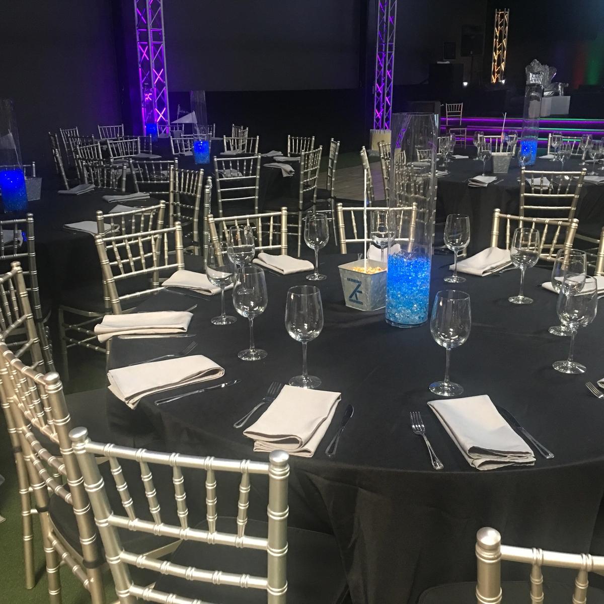 Black linens with gold chiavari chairs and blue centerpiece vases