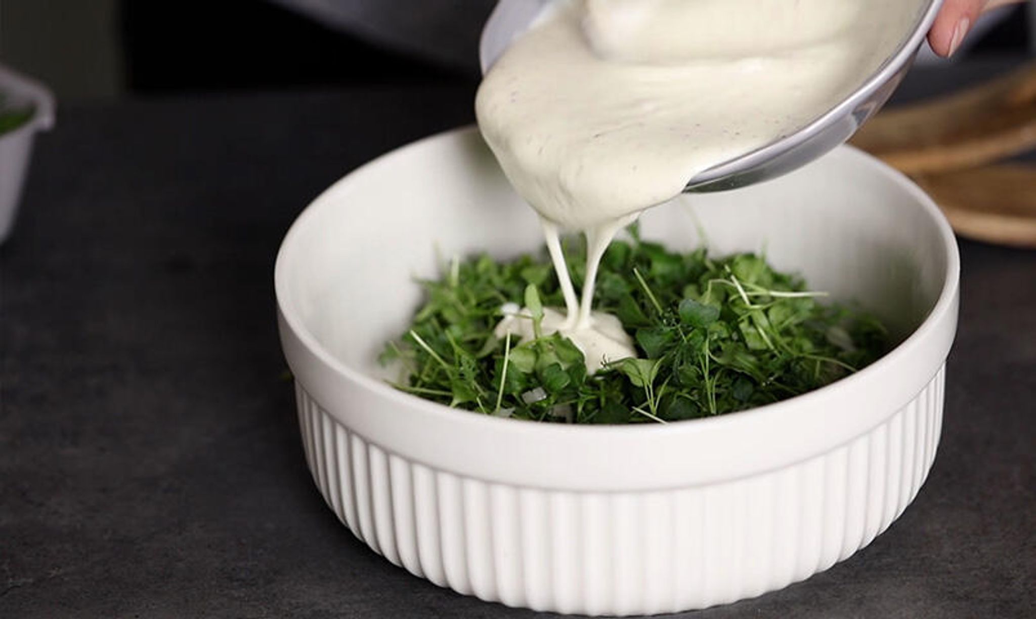 Skål med skördade mikroblad av grönkål och dressing som hälls över.