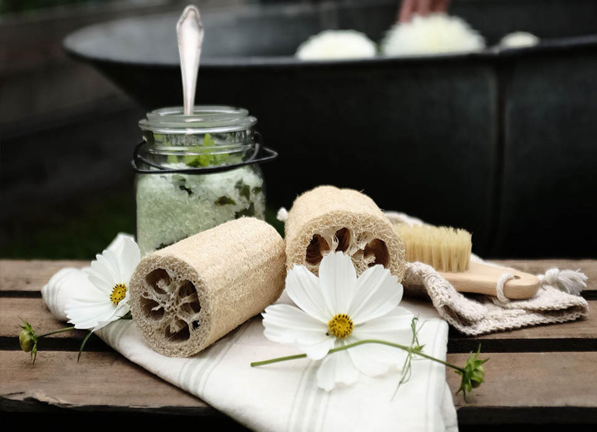 En person bak en krukke med hjemmelaget sukkerpeeling, blomster og en luffa.