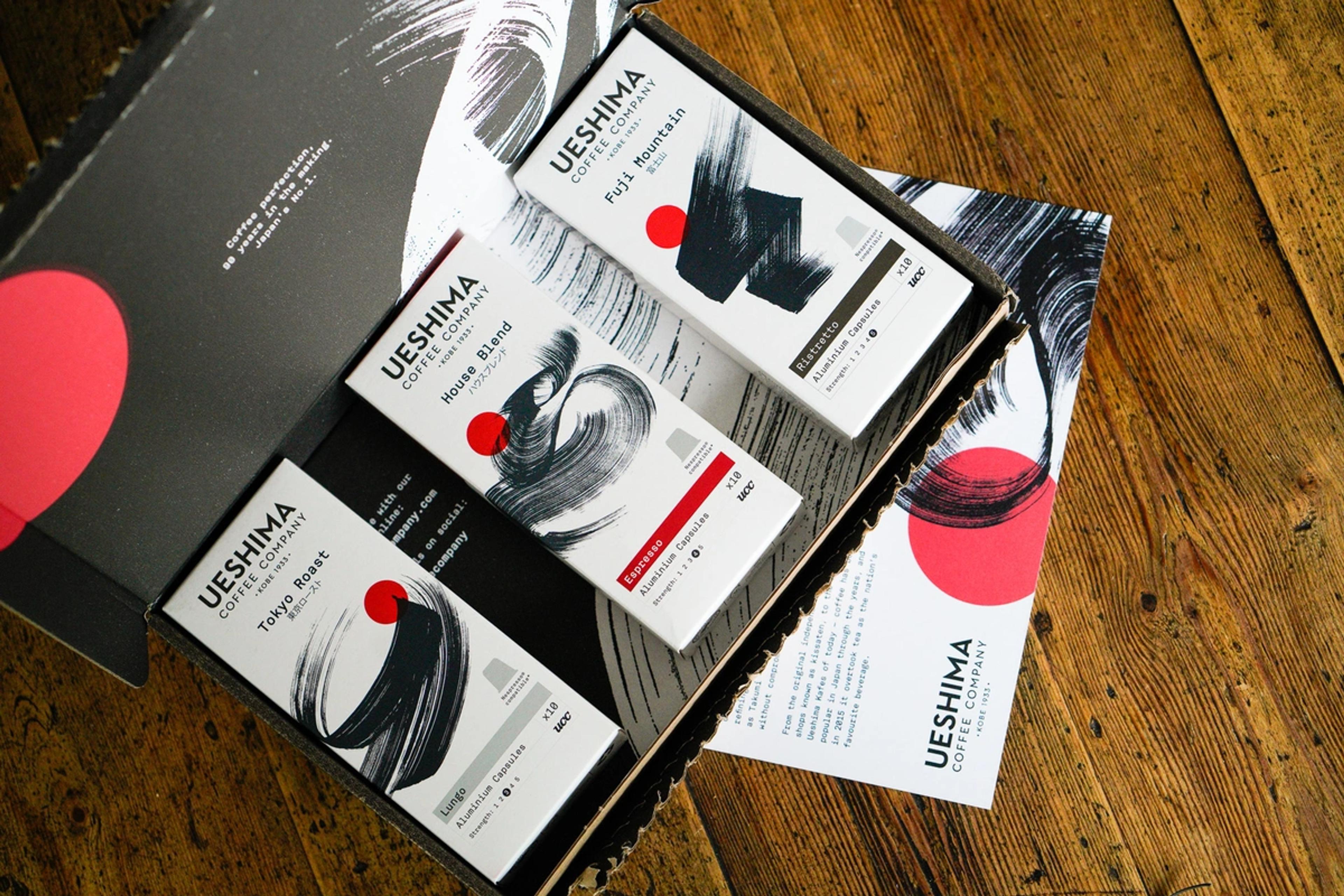 An open gift box of Ueshima Coffee Company aluminium capsules in Tokyo Roast, House Blend and Fuji Mountain on a wooden table.