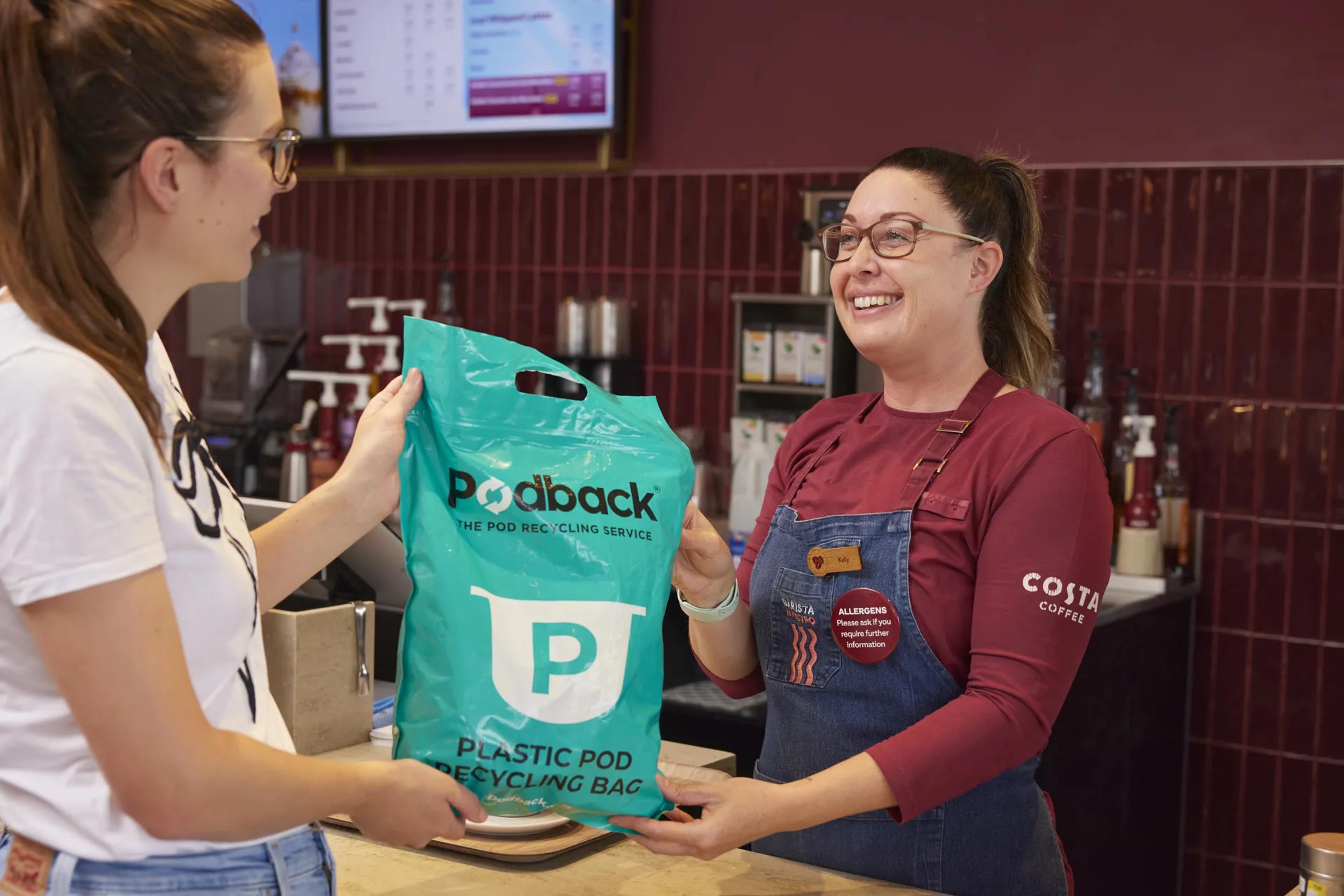 A Costa barista handing a customer a Podback plastic pod recycling bag over the counter