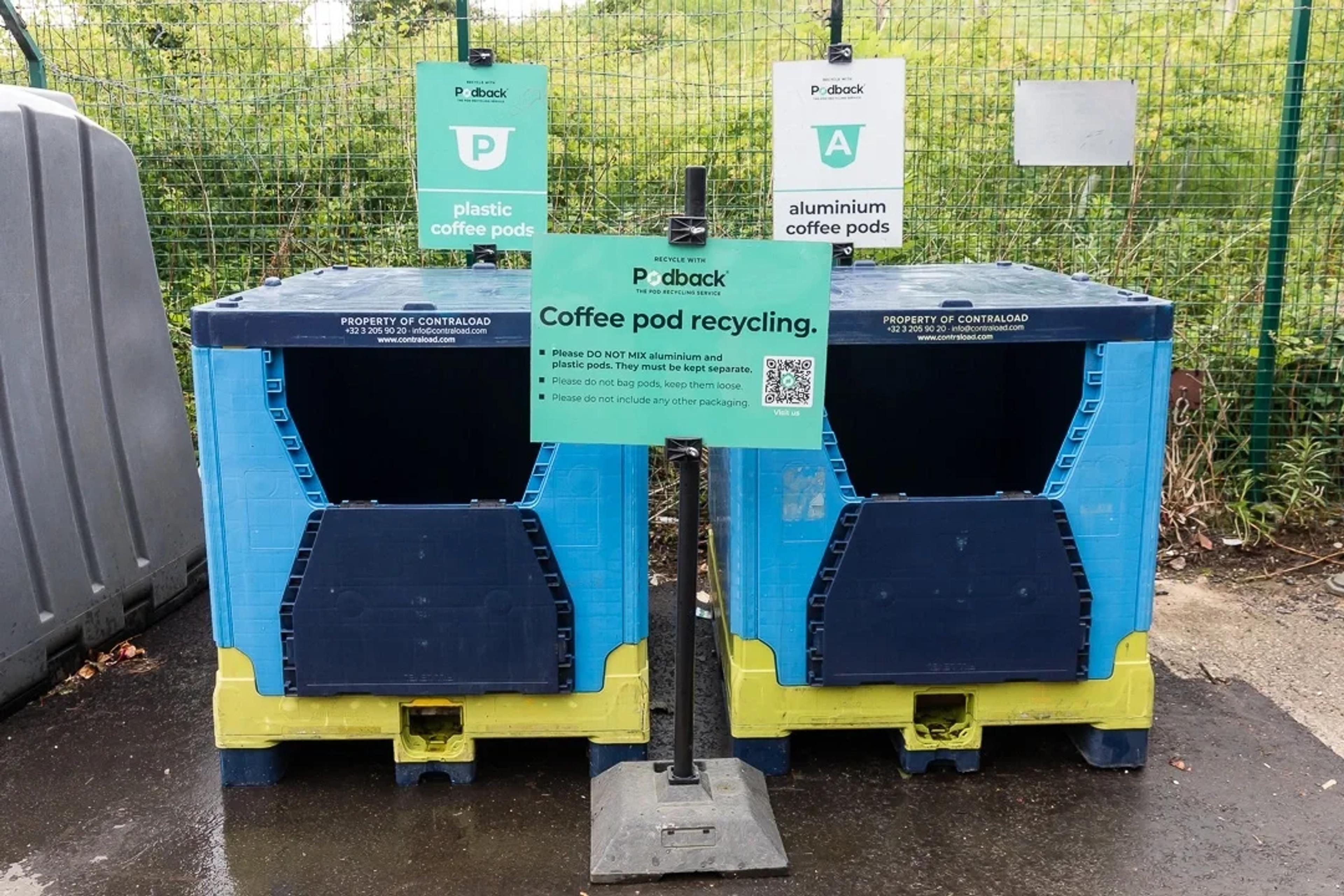 Two Podback containers at a household recycling centre, signed for plastic and for aluminium coffee pods, with a "Coffee pod recycling" sign asking residents to keep the two types separate and not to bag them.