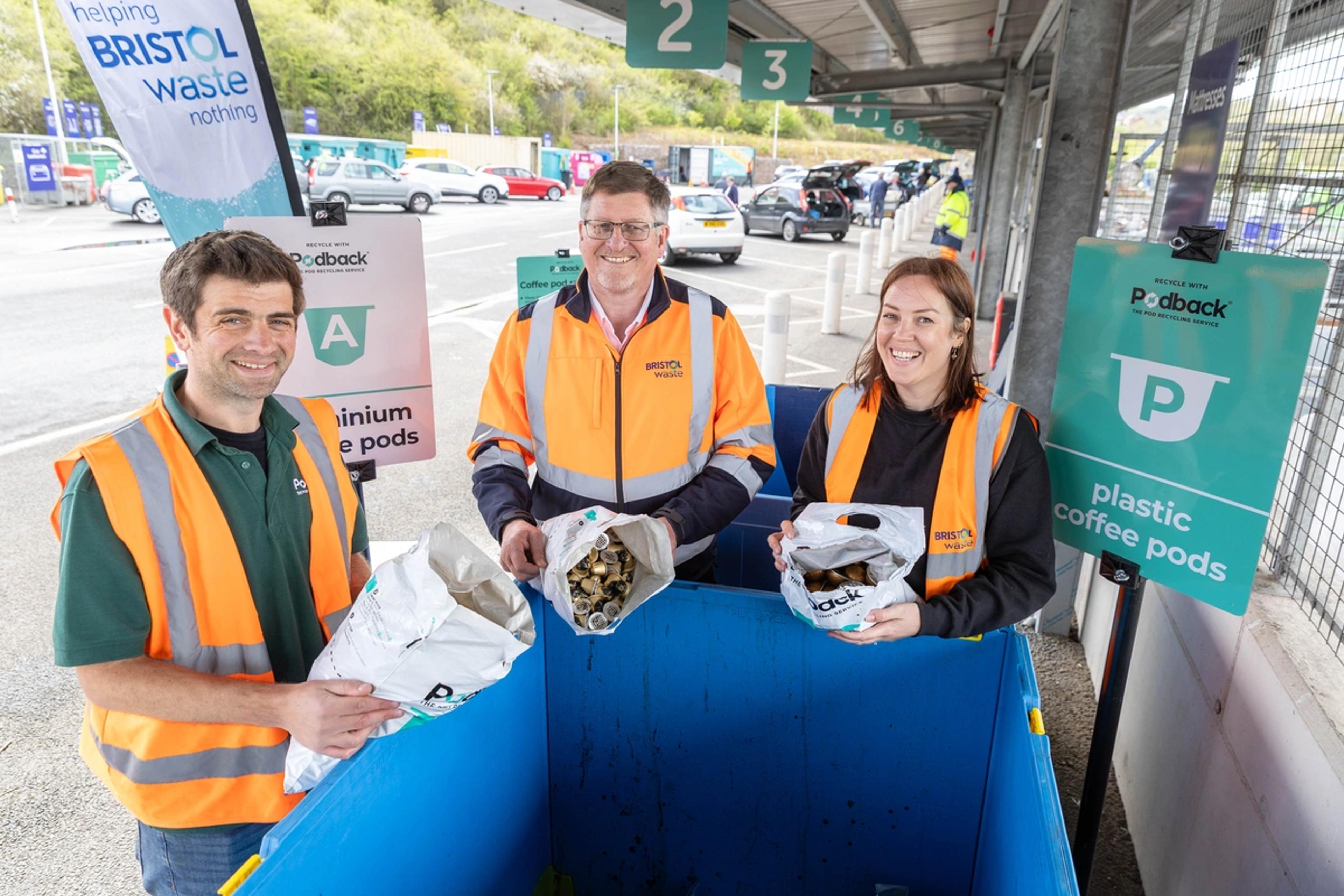 Three people in hi-vis are tipping used coffee pods into a container at a recycling centre