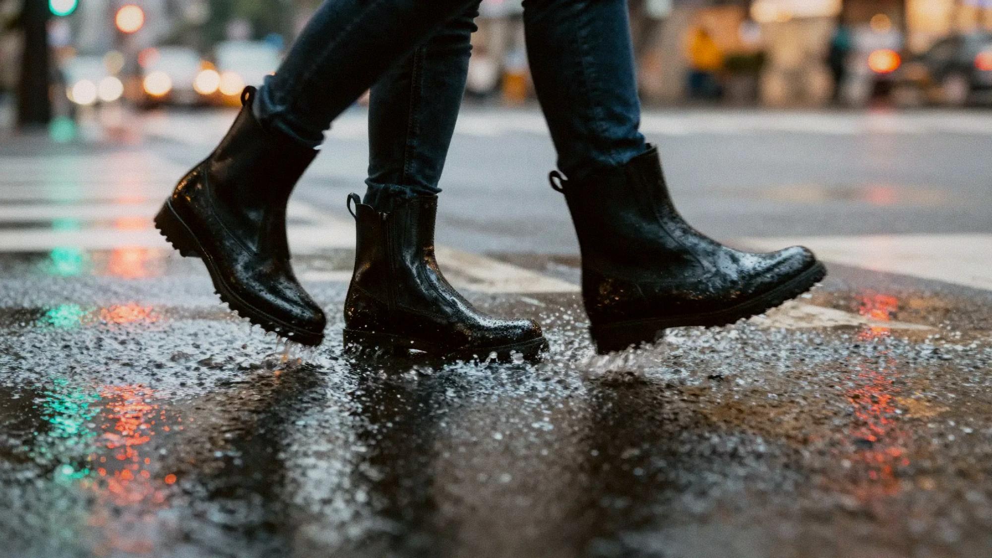 Close-up of waterproof black ankle boots stepping through a rain puddle on a Taipei crosswalk