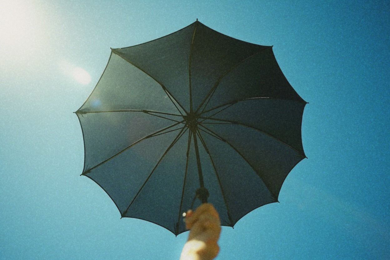 A black UV-coated parasol held open against a fierce blue summer sky, silver underside coating visible