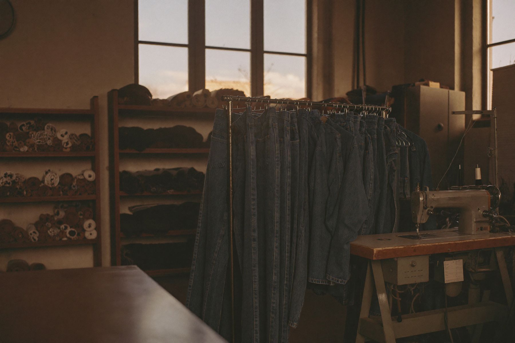 Rack of upcycled indigo denim beside bolts of fabric and an industrial sewing machine in a converted Taipei textile factory