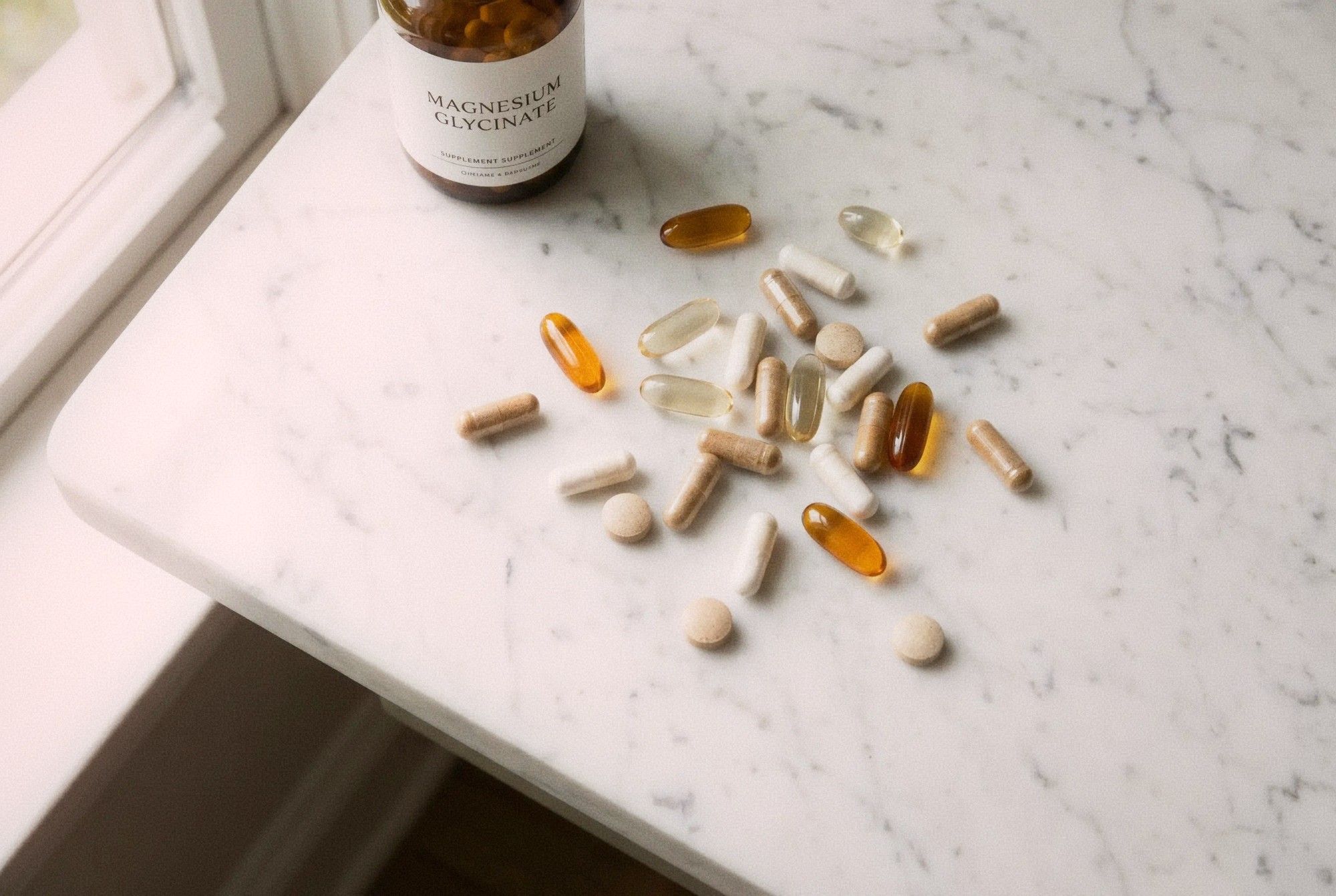 Various supplement capsules and tablets scattered on a white marble surface