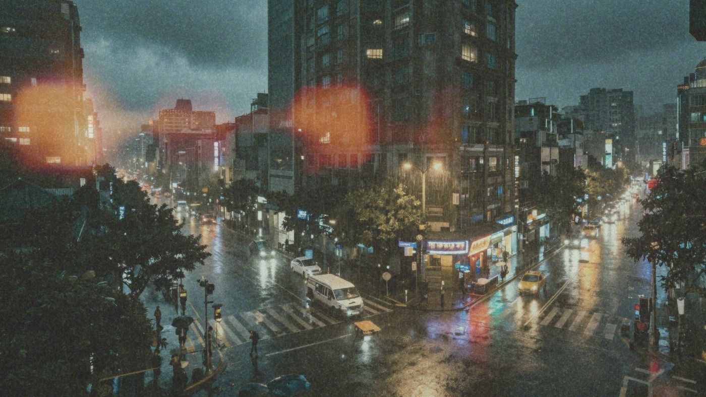 Elevated view of a rain-soaked city intersection at night, wet asphalt reflecting traffic lights