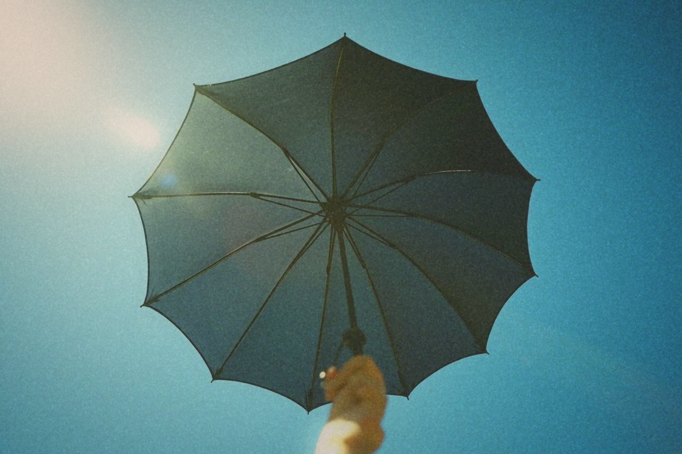 A black UV-coated parasol held open against a fierce blue summer sky, silver underside coating visible