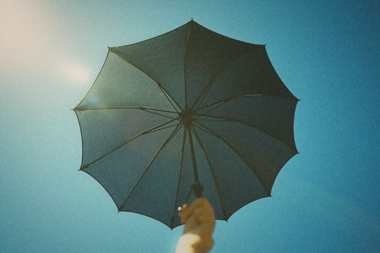 A black UV-coated parasol held open against a fierce blue summer sky, silver underside coating visible