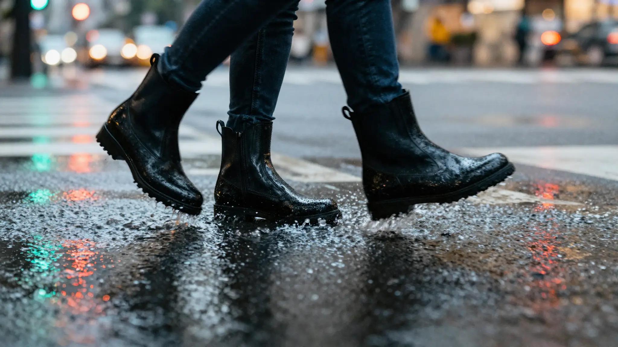 Close-up of waterproof black ankle boots stepping through a rain puddle on a Taipei crosswalk