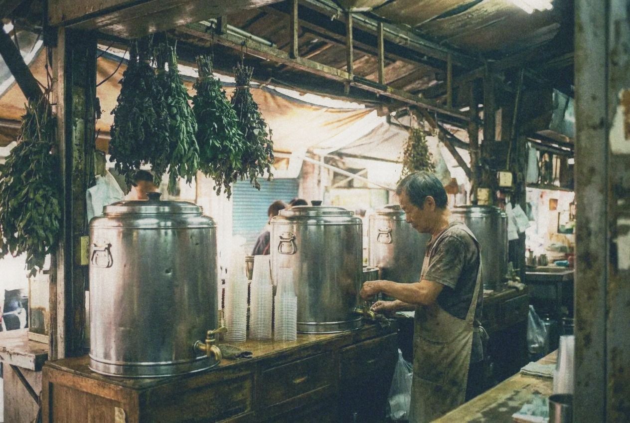 A herbal tea stall with large steel urns and stacks of plastic cups at a Taipei market