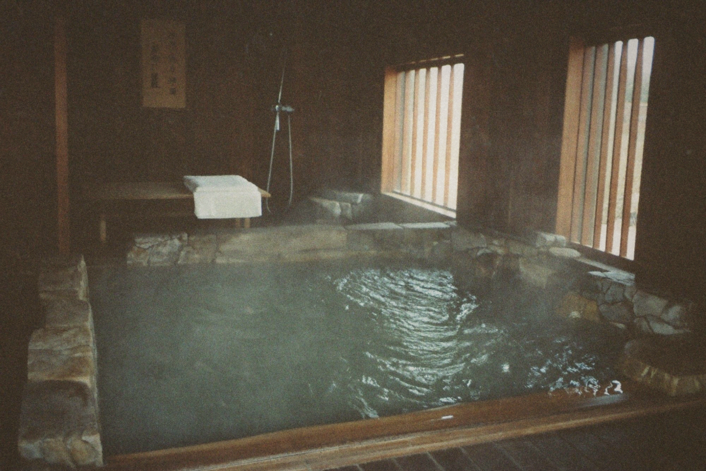 Dimly lit stone hot spring bath filled with steaming water in a traditional spa room