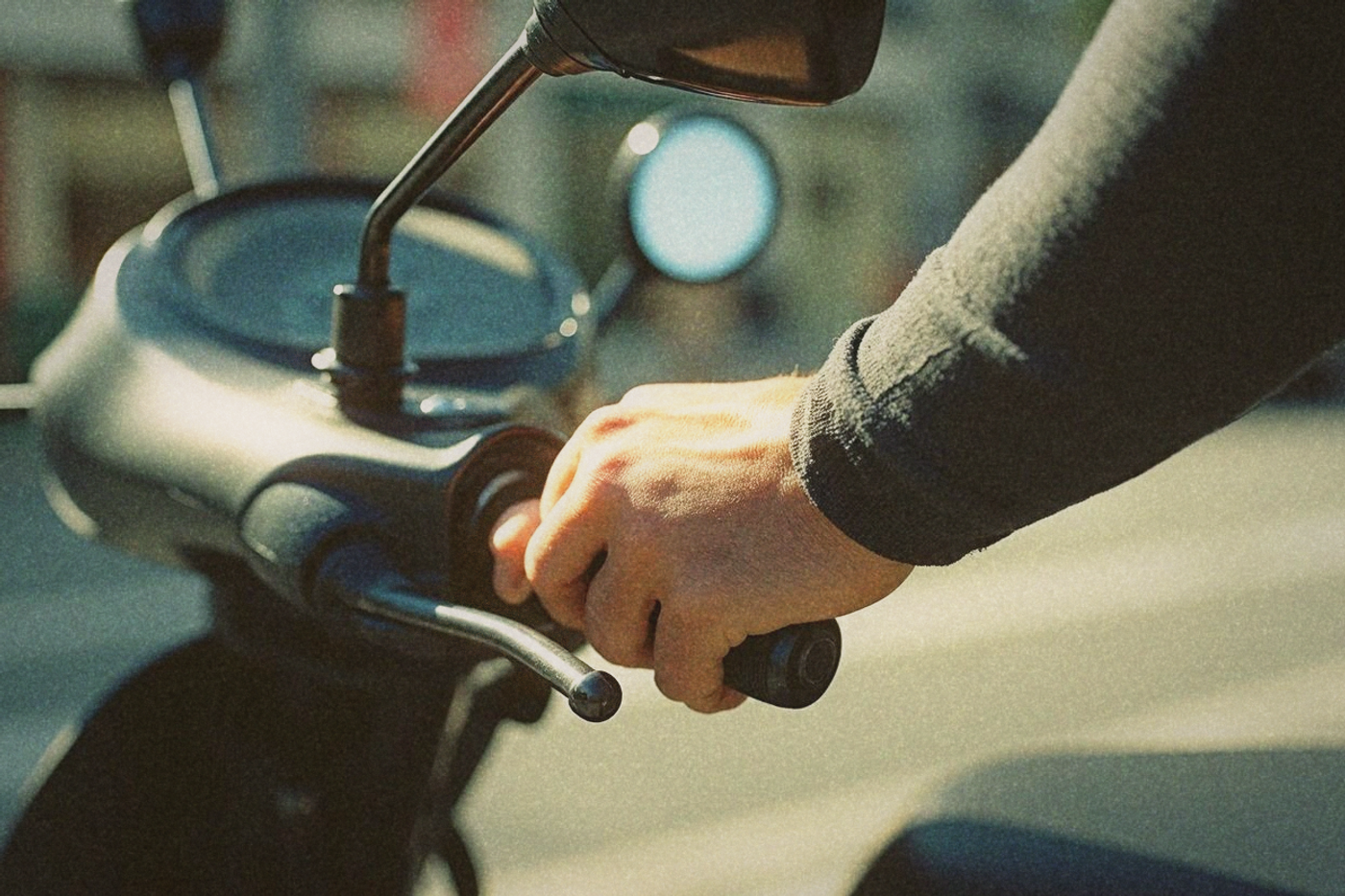 Close-up of a forearm in charcoal UV arm sleeves gripping a scooter handlebar in bright Taipei sunlight