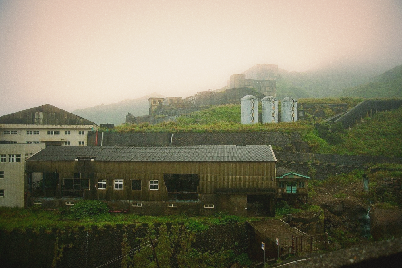 Derelict mine buildings and concrete silos on a misty green hillside