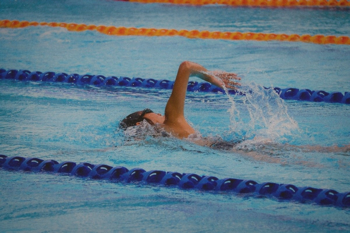 Swimmer doing front crawl in an indoor pool between blue and orange lane ropes