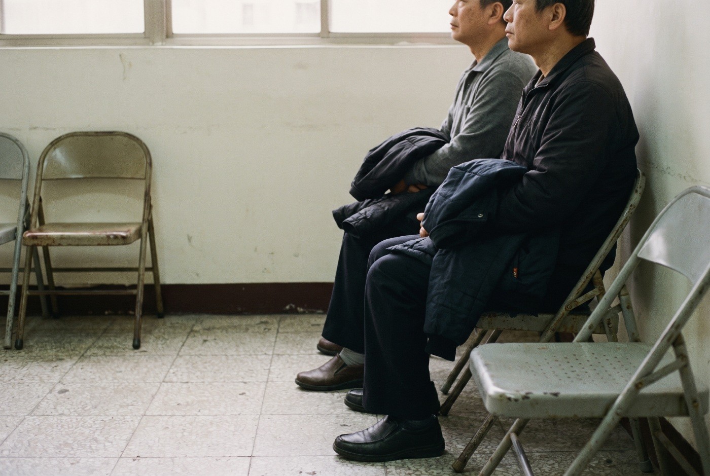 Illustration: People waiting on simple folding chairs.