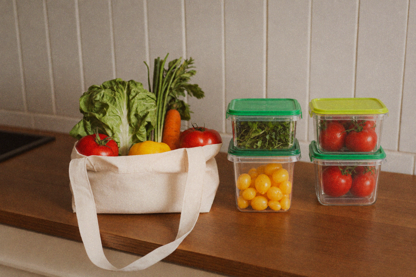 Reusable shopping bag and food containers filled with fresh market vegetables on a kitchen counter