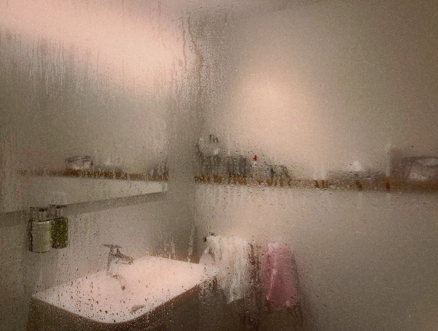 A small Taipei apartment bathroom with condensation on the mirror and toiletries crowded on limited surfaces