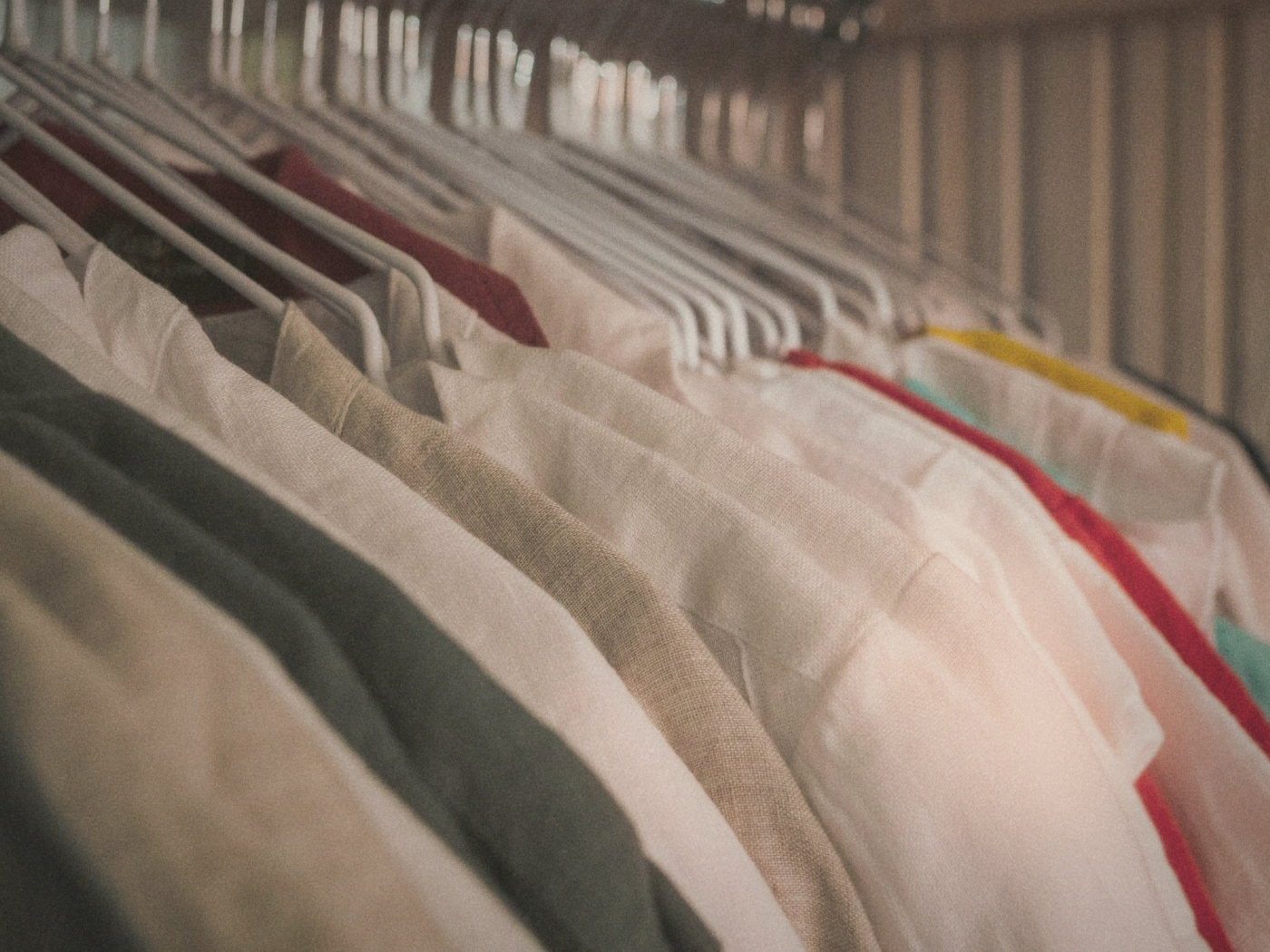 Row of linen shirts in cream, olive and pink hanging closely together on wire hangers