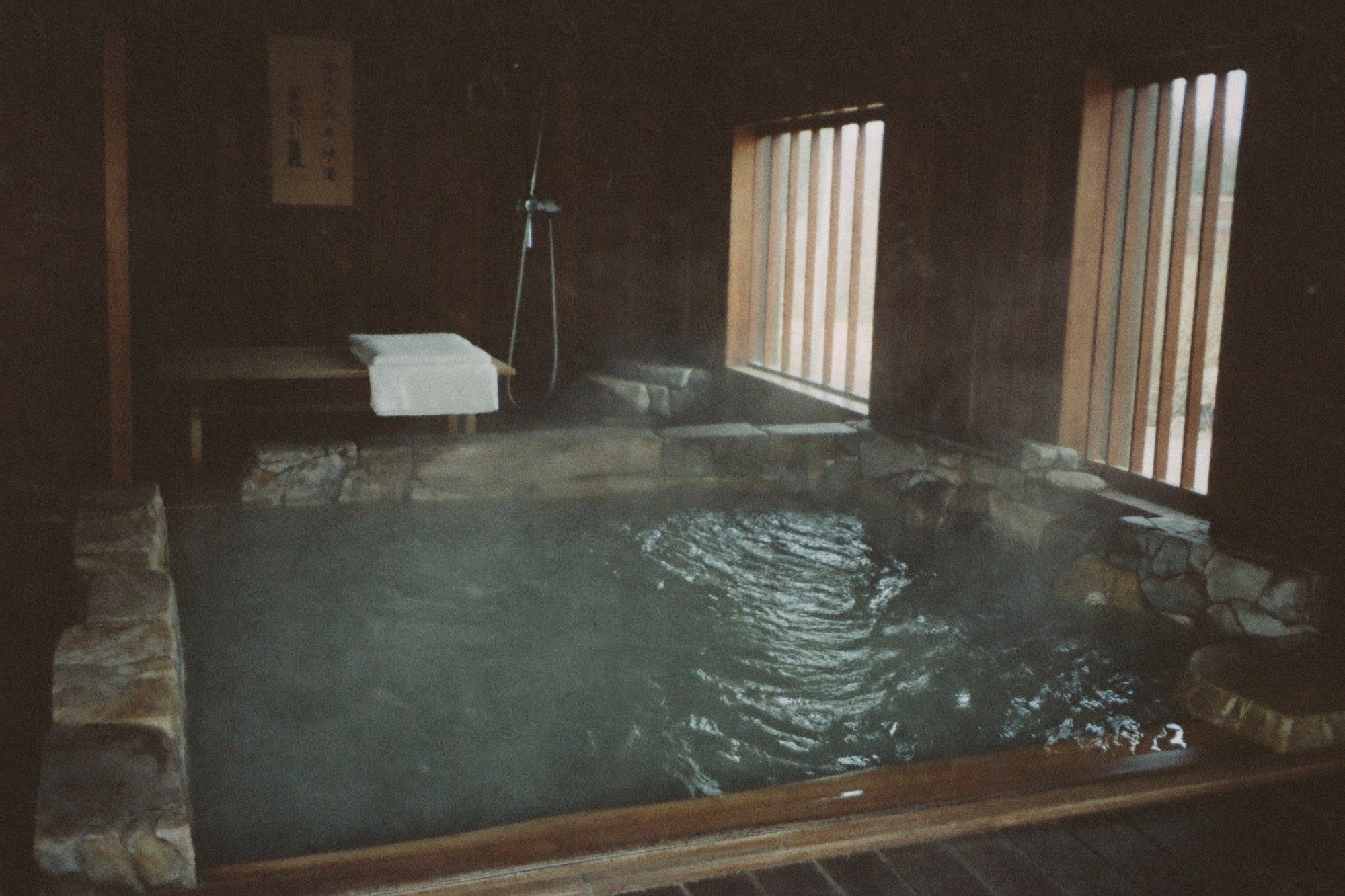 Dimly lit stone hot spring bath filled with steaming water in a traditional spa room