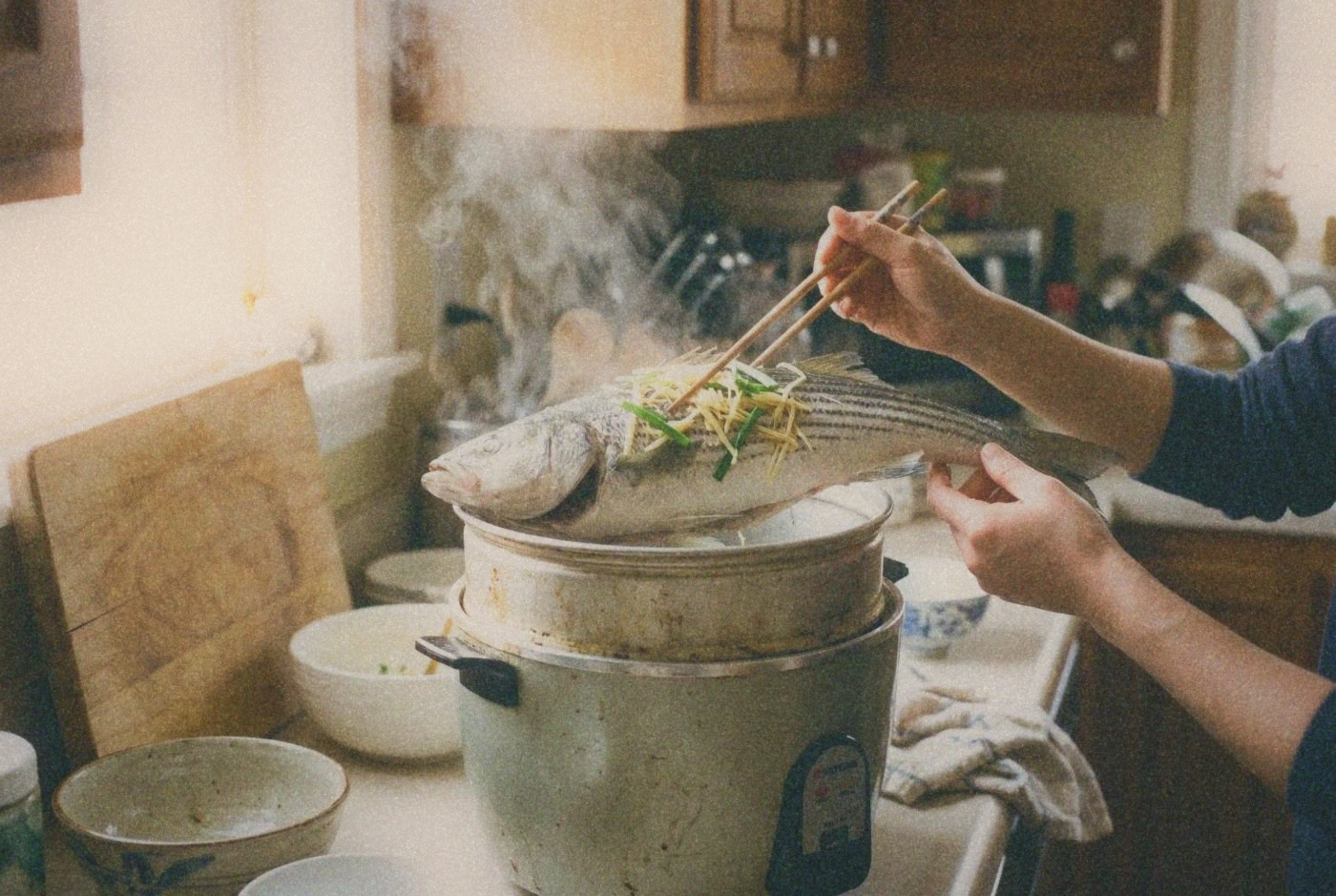 Whole steamed fish with ginger and scallions being lifted from inside a Tatung rice cooker inner pot