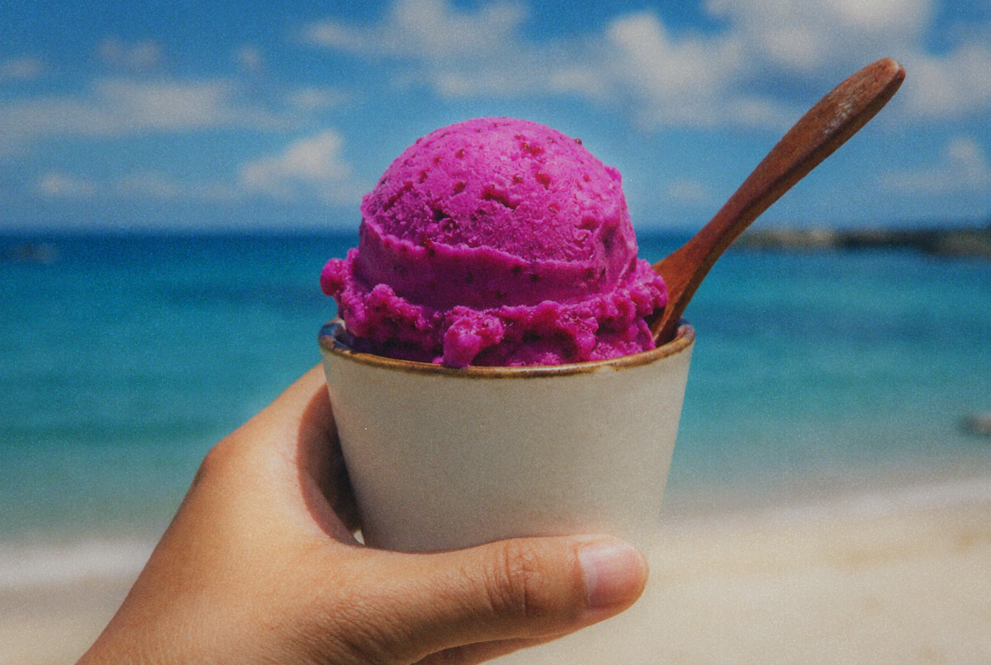 Bright pink-purple scoop of prickly pear cactus ice cream held against ocean background