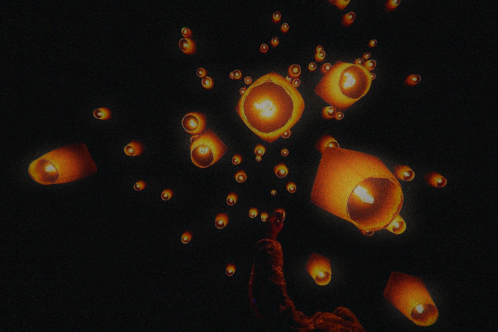 Sky lanterns drifting upward against a black night sky above a single raised hand